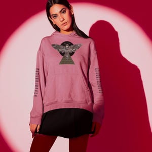 以下が含まれることがあります： 前面に大きな蛾のグラフィック、黒い円とピラミッドをあしらった、くすんだバラ色のパーカー。袖にはバイナリコードがプリントされています。パーカーにはフロントポケットとフードが付いています。