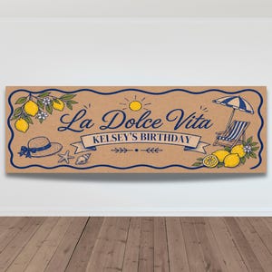 May include: A rectangular banner with a brown background and blue border. The banner features the text "La Dolce Vita" and "Kelsey's Birthday". Illustrations include lemons, a sun, a beach umbrella, a beach chair, a hat, a starfish, and a seashell.