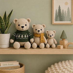 May include: Three beige crocheted teddy bears of varying sizes arranged in a row. The largest bear wears a dark green sweater with a white tree pattern. The middle bear wears a mustard yellow scarf. The smallest bear has no accessories.