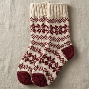 Könnte beinhalten: Ein Paar gestrickte Socken mit cremefarbenem Grund und einem sich wiederholenden Muster aus bordeauxfarbenen floralen Designs. Die Bündchen und Zehen sind einfarbig bordeaux. Die Socken sind aus dickem, warmem Material.