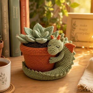 May include: A crocheted light green dragon with orange accents hugging a terracotta-colored crocheted pot containing a crocheted light green succulent plant. The dragon has closed eyes and a long tail that wraps around the base of the pot.