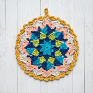 Puede incluir: Un salvamanteles redondo y colorido tejido a crochet con un diseño floral. El centro es turquesa, rodeado de formas verdes, azul marino y azul verdoso. Los bordes exteriores presentan melocotón, gris y amarillo mostaza. Un pequeño lazo en la parte superior para colgar.