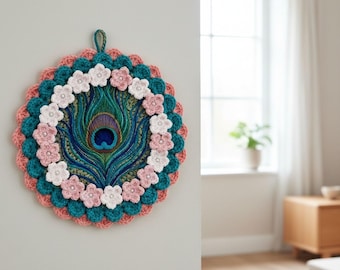 Könnte beinhalten: Handgefertigte Wanddekoration mit Pfauenfeder. Das kreisförmige Design zeigt eine zentrale Pfauenfeder, umgeben von teal-, korallen- und weißen Häkeldetails. Rosa und weiße Häkelblumen sind um die Feder angeordnet.