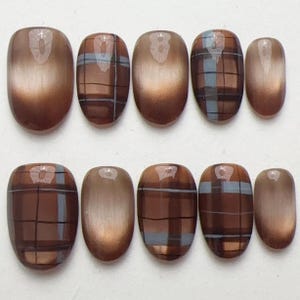 May include: A set of ten press-on nails in varying sizes, featuring a glossy brown finish. Some nails have a solid metallic brown appearance, while others display a brown and light blue plaid pattern with thin horizontal and vertical lines.
