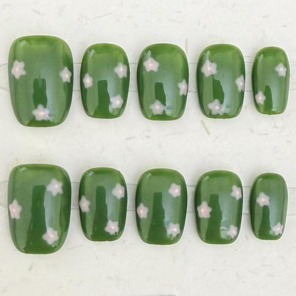 May include: A set of ten press-on nails in a glossy olive green finish, each featuring a repeating pattern of small, pale pink five-petaled flowers. The nails are arranged in two rows of five, varying in size from wide to narrow, with rounded edges.