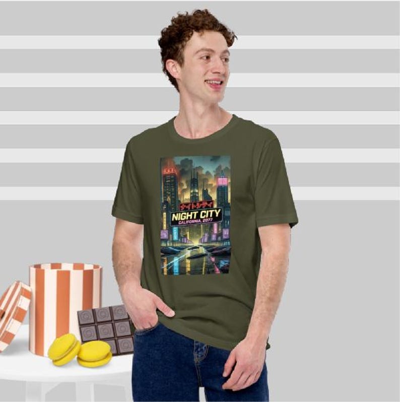 Op de afbeelding: Olijfgroen t-shirt met een levendige afbeelding van een futuristische stad met de tekst "NIGHT CITY CALIFORNIA 2077". Het ontwerp toont neonlichten en hoge gebouwen. Het t-shirt wordt door een persoon gedragen.