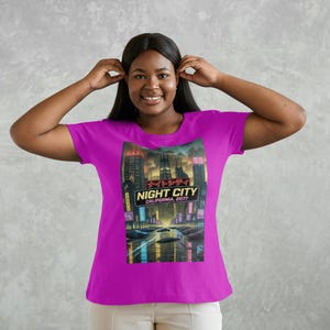 Op de afbeelding: Magenta T-shirt met een afbeelding van een futuristische stadsgezicht met de tekst "NIGHT CITY CALIFORNIA 2077". Het ontwerp bevat neonlichten en een auto op een weg.