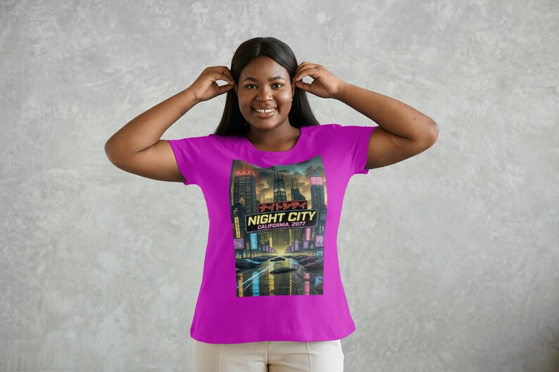 Op de afbeelding: Magenta T-shirt met een afbeelding van een futuristische stadsgezicht met de tekst "NIGHT CITY CALIFORNIA 2077". Het ontwerp bevat neonlichten en een auto op een weg.