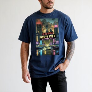 Op de afbeelding: Marineblauw T-shirt met een levendige afbeelding van een futuristisch stadslandschap 's nachts. Het ontwerp bevat neonreclame, wolkenkrabbers en de tekst "NIGHT CITY CALIFORNIA, 2077". Het shirt heeft een klassieke ronde hals.
