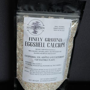 May include: A clear plastic bag containing finely ground eggshell calcium for vegetable plants. The label reads "Hallthorn" and "Finely Ground Eggshell Calcium." The net weight is 16 ounces (1 pound).