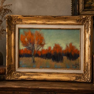 May include: A landscape painting in a rectangular gold ornate frame featuring a row of trees with vibrant orange foliage against a muted teal sky. The artwork depicts a field with dark shadows and a single prominent tree in the foreground.
