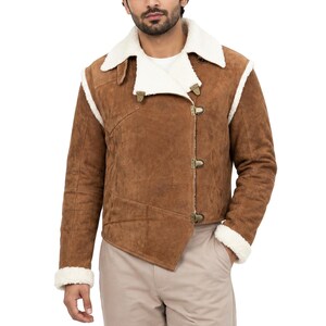 Könnte beinhalten: Eine braune Wildlederjacke mit weißem Kunstfellfutter, ausgestattet mit einem asymmetrischen Frontverschluss durch drei Metallschnallen, einem breiten Reverskragen und langen Ärmeln mit weißen Kunstfellbündchen, getragen über beigen Hosen.