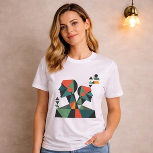 May include: White crew neck t-shirt with a geometric design. The design features two stylized human profiles in red, green, and orange. The design includes triangles and other geometric shapes. The shirt is a crew neck style.