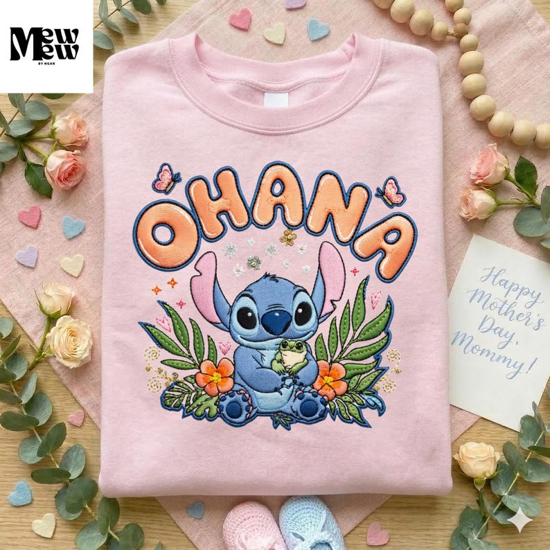 A pink t-shirt with a cartoon character and floral design, surrounded by various decorative items such as flowers, beads, and a note.