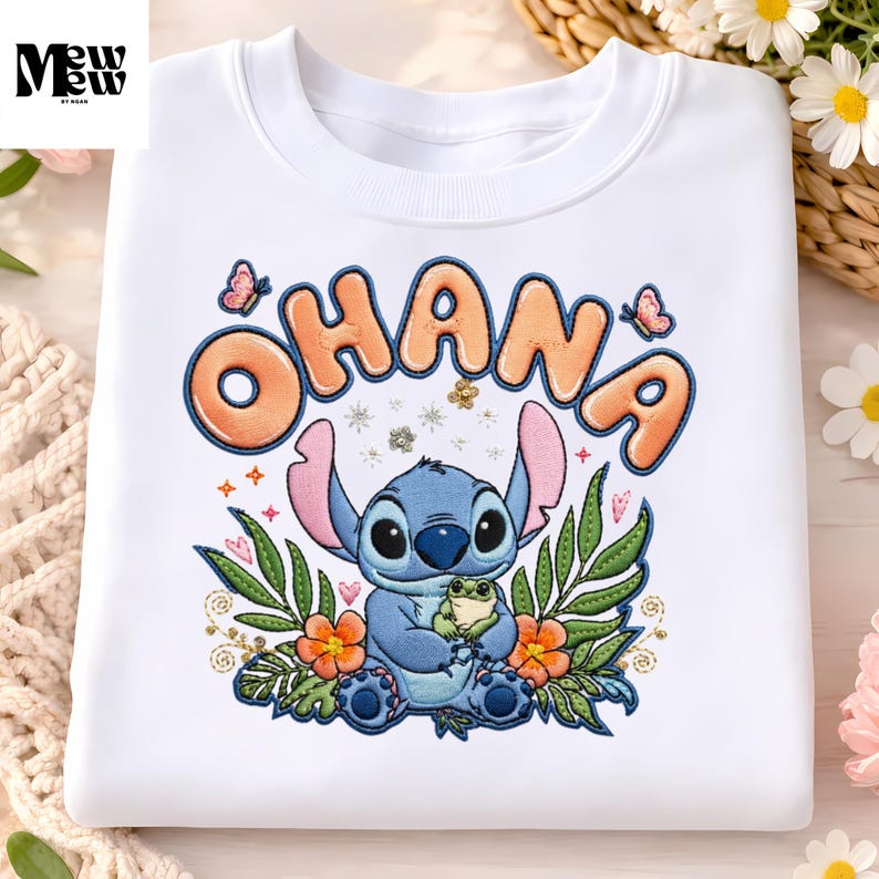 A white t-shirt with a colorful embroidered design featuring a character from the Disney animated film "Stitch" surrounded by flowers and butterflies.