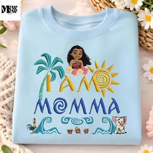 A light blue t-shirt with a colorful design featuring a cartoon character, a sun, palm trees, and various other elements.