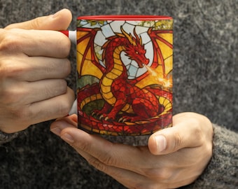 May include: A ceramic mug with a red interior and a wrap-around graphic featuring a red dragon in a stained-glass style. The dragon is depicted with wings spread, breathing a small flame, set against a yellow and white geometric background.
