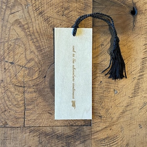 May include: A wooden bookmark with a black tassel. The bookmark has the text "and so the adventure continues" written on it.