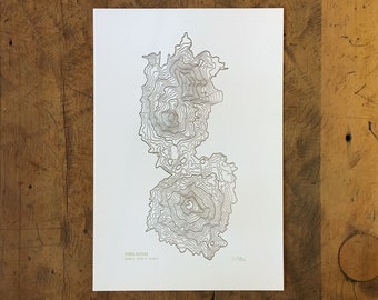 May include: A black and white topographic map print of Three Sisters, Oregon. The print shows the elevation contours of the mountain range. The text "Three Sisters, 12,053' - 10,350'" is printed at the bottom of the print.