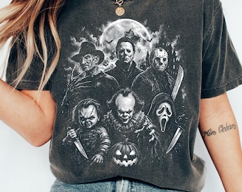 Puede incluir: Una camiseta gris carbón de manga corta con un estampado gráfico detallado de cinco personajes icónicos de películas de terror. El diseño incluye una luna llena, un castillo espeluznante y una calabaza, todo en un estilo monocromático y desgastado.