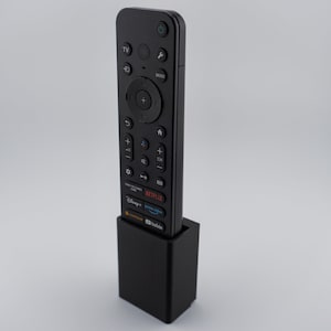May include: A black TV remote control with various buttons, including power, volume, and channel controls, is placed in a black rectangular stand. The remote has streaming service buttons for Netflix, Disney+, and YouTube.