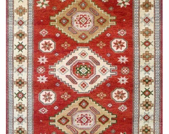 May include: A rectangular red rug with a central geometric design in beige, brown, and white. The rug features a border with repeating floral and geometric patterns in complementary colors. The rug is a traditional style.