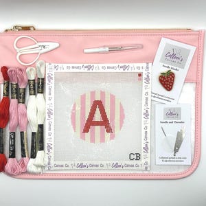 May include: A pink canvas kit with embroidery supplies. Includes scissors, needles, thread, and a canvas with a pink and white striped circle and the letter "A". A strawberry pin and cards are also included.