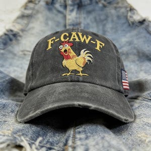 May include: A distressed black baseball cap with the embroidered text "F-CAW-F" above a cartoon rooster. The rooster is yellow, red, and white. An American flag patch is on the side of the cap.