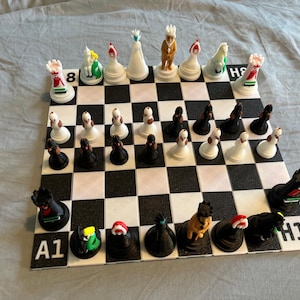 Puede incluir: Un juego de ajedrez completo con un tablero a cuadros blanco y negro. Las piezas de ajedrez están diseñadas de forma única con varios colores y formas, incluyendo torres, caballos, alfiles, un rey y una reina. El tablero está etiquetado con letras y números.