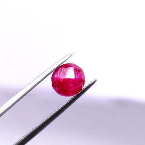 Può includere: Una gemma rotonda e sfaccettata di colore rosso vibrante tenuta da una pinzetta in metallo color argento. La pietra presenta una superficie lucida con molteplici sfaccettature geometriche che riflettono la luce, mostrando un colore cremisi saturo.