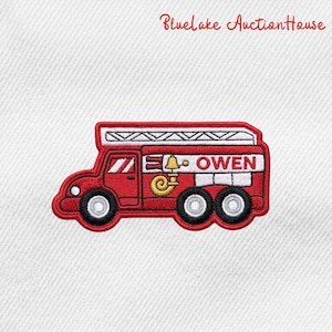 May include: Red fire truck patch with the name "OWEN" on the side. The patch has a white ladder on top and a gold bell and hose detail. The patch is embroidered on a white background.