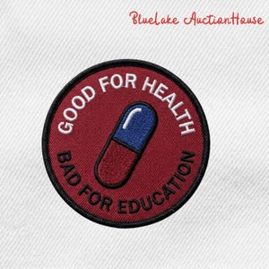 May include: A round, embroidered patch with the text "GOOD FOR HEALTH" and "BAD FOR EDUCATION" in white. A blue and red capsule is in the center. The patch has a black border and is on a white background.