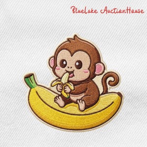 May include: Embroidered patch featuring a cartoon monkey sitting on a yellow banana and eating a banana. The monkey is brown with pink ears and cheeks. The text "Bluelake AuctionHouse" is in the upper right corner.