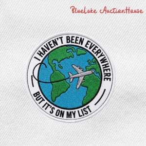 May include: Embroidered patch with the text "I HAVEN'T BEEN EVERYWHERE BUT IT'S ON MY LIST". The patch features a blue and green globe with a white airplane and a black outline.
