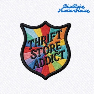May include: A shield-shaped embroidered patch featuring a vibrant rainbow sunburst pattern in red, orange, yellow, green, blue, and purple. The black text "THRIFT STORE ADDICT" is stitched across the center in a bold, sans-serif font.