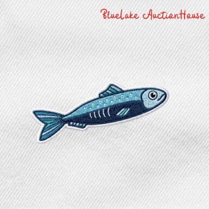 May include: Embroidered patch of a blue fish with white accents. The fish has a detailed design, including scales, fins, and a tail. The text "Bluelake AuctionHouse" is in red script at the top.