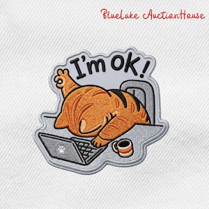 May include: Embroidered patch featuring an orange cat with black stripes, lying on a desk with a laptop and coffee cup. The text "I'm ok!" is above the cat. The patch has a gray border and is on a white background.