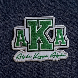 May include: Embroidered patch featuring the letters "AKA" in green, with a white border and the words "Alpha Kappa Alpha" in cursive. The patch is set against a dark blue fabric background.