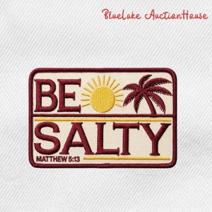 May include: Embroidered patch with the words "BE SALTY" in burgundy letters, a yellow sun, and a burgundy palm tree. The text "MATTHEW 5:13" is below "SALTY". The patch is rectangular with a burgundy border.