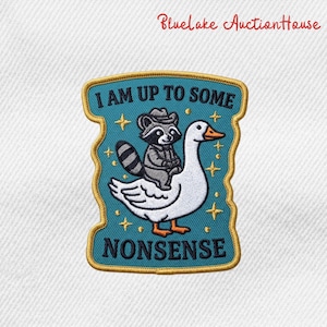May include: Embroidered patch featuring a raccoon in a cowboy hat riding a goose. The patch has a teal background with gold trim and the text "I AM UP TO SOME NONSENSE". Stars are scattered around the raccoon and goose.