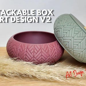 Może przedstawiać: Pudełko do układania w stosy art design V2 z okrągłą, ciemnoróżową podstawą i szałwiowo-zieloną pokrywką z geometrycznym wzorem w jodełkę oraz małym drewnianym uchwytem. Widoczny jest tekst STACKABLE BOX ART DESIGN V2 oraz Art Design 3D.