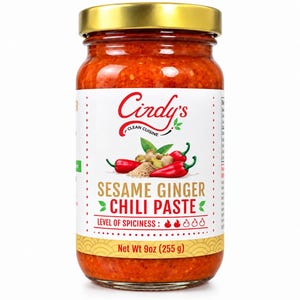 May include: A glass jar of Cindy's Clean Cuisine Sesame Ginger Chili Paste with a gold lid. The white label features red chili peppers, ginger root, and sesame seeds. The text reads Sesame Ginger Chili Paste, Net Wt 9oz (255 g), and Level of Spiciness.