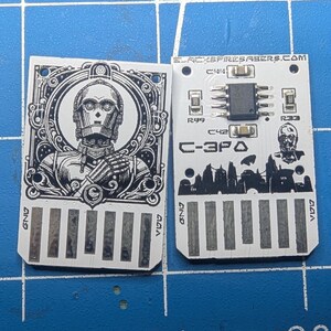 May include: Two rectangular circuit boards with C-3PO graphics. One board features a detailed C-3PO portrait within an ornate frame. The other board has the text "C-3PO" and a silhouette of a cityscape. The website "BLACKSPIRESABERS.COM" is printed on the board.