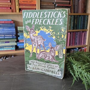 May include: A vintage book titled "Fiddlesticks and Freckles" with a cover illustration of two fawns in a forest setting. The book's title is in large, green letters, and the author's name is Sam Campbell.