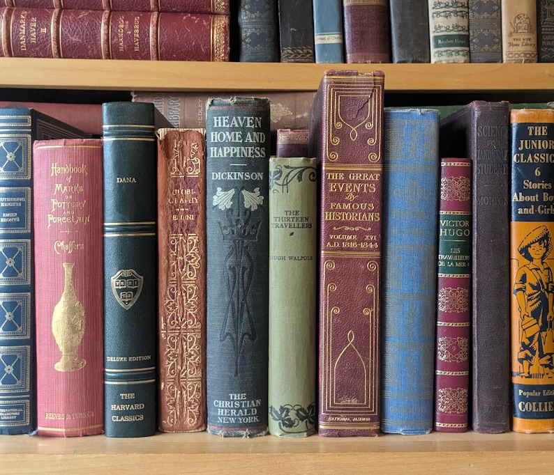 Puede incluir: Una colecci&oacute;n de libros antiguos en una estanter&iacute;a de madera. Los lomos muestran t&iacute;tulos como "Heaven Home and Happiness" y "The Great Events". Los colores var&iacute;an desde rojos y azules intensos hasta verdes y marrones apagados. Los libros var&iacute;an en tama&ntilde;o y encuadernaci&oacute;n.