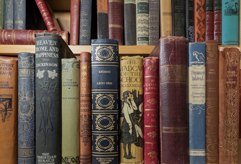 Puede incluir: Una colecci&oacute;n de libros antiguos con varios colores y texturas. Los t&iacute;tulos incluyen "Heaven Home and Happiness", "Exodus" y "Treasure Island". Las espinas muestran elementos decorativos y papel envejecido, creando una est&eacute;tica vintage.