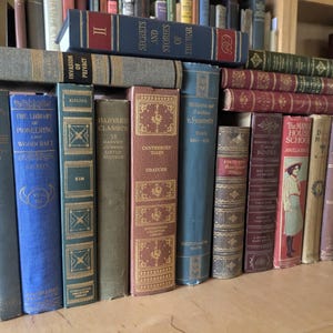 Könnte beinhalten: Eine Sammlung antiker Bücher mit verschiedenen Farben und Designs. Die Buchrücken zeigen Titel wie "Hunter Hom", "The Library of Pioneering" und "Harvard Classics". Einige Bücher sind gestapelt und zeigen eine Vielzahl von Größen und Einbandstilen.