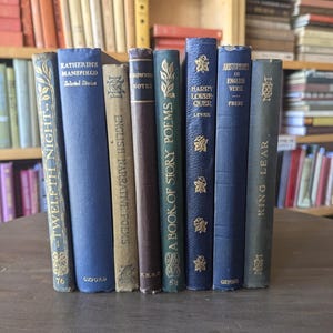 May include: A collection of vintage books with various colored spines, including titles like "Twelfth Night" and "Katherine Mansfield." The books are arranged on a wooden surface, with a bookshelf in the background.