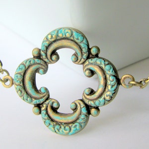 May include: A gold necklace with a turquoise blue pendant in the shape of a four-leaf clover. The pendant has a detailed, ornate design.