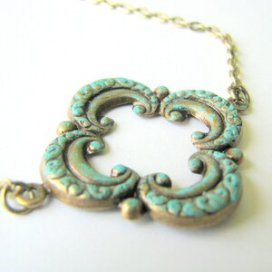 May include: A turquoise and gold necklace with a decorative, ornate pendant. The pendant is shaped like a four-leaf clover with a detailed, swirling design.